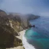 Photographie Big Sur - Californie Photographie artistique des falaises escarpées de Big Sur en Californie avec plage isolée et eaux turquoise de l'océan Pacifique sous un ciel brumeux, tirage d'art paysage marin