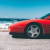 Photographie Ferrari Testa Rossa Spider Photographie artistique d'une Ferrari Testarossa Spider rouge stationnée au bord de l'océan Pacifique en Californie, avec vagues et rochers en arrière-plan sous un ciel bleu azur, tirage d'art automobile limité