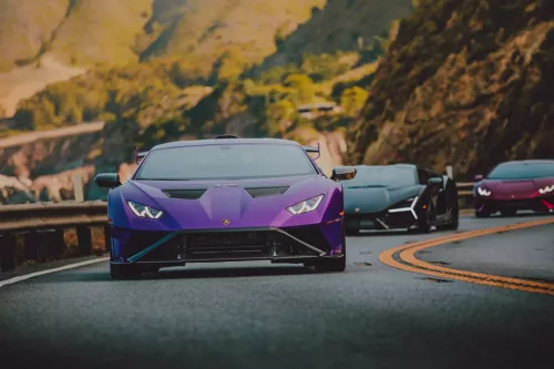 Photographie Lamborghini Party Photographie artistique d'un convoi de Lamborghini sur route sinueuse de montagne, avec une Huracán violette en premier plan suivie de plusieurs supercars italiennes