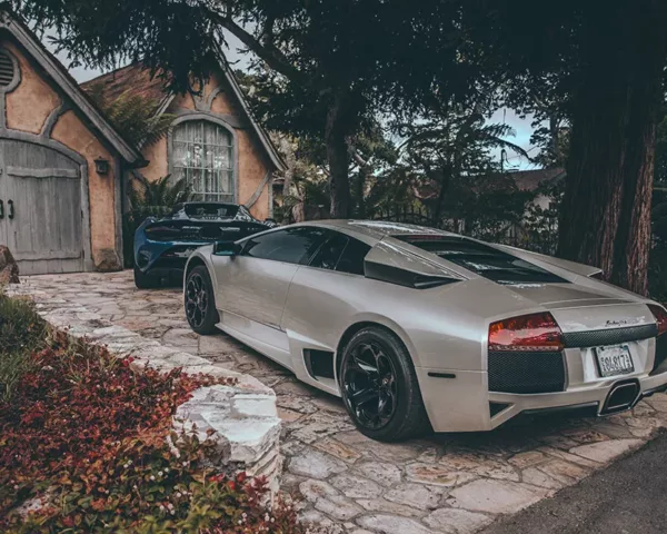 Photographie Lamborghini et McLaren Photographie artistique d'une Lamborghini argentée et d'une McLaren bleue devant un cottage rustique, contraste entre supercars modernes et architecture traditionnelle, tirage d'art automobile de luxe