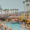 Photo The Saguaro Palm Springs Photographie artistique de l'hôtel The Saguaro à Palm Springs avec sa façade multicolore, sa piscine turquoise, ses parasols jaunes et ses palmiers sous le ciel bleu californien