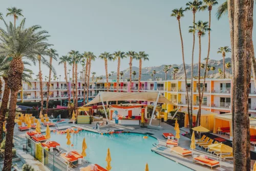 Photo The Saguaro Palm Springs Photographie artistique de l'hôtel The Saguaro à Palm Springs avec sa façade multicolore, sa piscine turquoise, ses parasols jaunes et ses palmiers sous le ciel bleu californien
