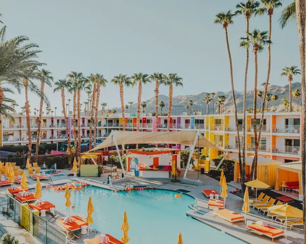 Photo The Saguaro Palm Springs Photographie artistique de l'hôtel The Saguaro à Palm Springs avec sa façade multicolore, sa piscine turquoise, ses parasols jaunes et ses palmiers sous le ciel bleu californien