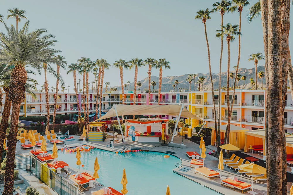 Photographie artistique de l'hôtel The Saguaro à Palm Springs avec sa façade multicolore, sa piscine turquoise, ses parasols jaunes et ses palmiers sous le ciel bleu californien