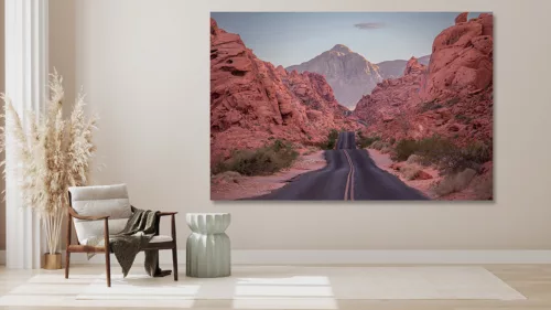 Photographie artistique de la route sinueuse traversant les formations rocheuses rouges de la Valley of Fire au Nevada, avec montagnes majestueuses au coucher du soleil
