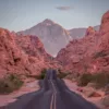 Photographie Valley Of Fire Photographie artistique de la route sinueuse traversant les formations rocheuses rouges de la Valley of Fire au Nevada, avec montagnes majestueuses au coucher du soleil