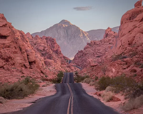 Photographie Valley Of Fire Photographie artistique de la route sinueuse traversant les formations rocheuses rouges de la Valley of Fire au Nevada, avec montagnes majestueuses au coucher du soleil