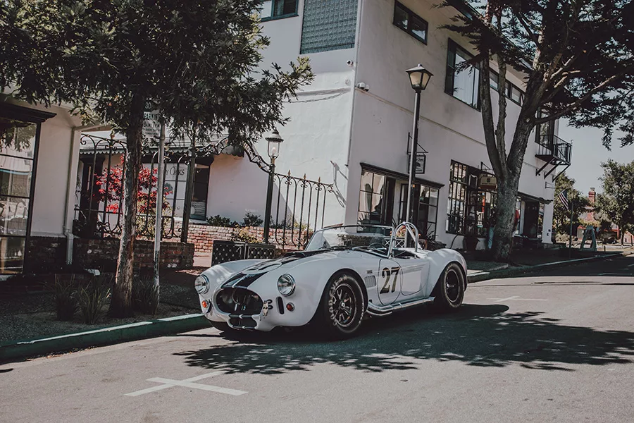 Photographie artistique d'une Shelby Cobra 427 blanche avec bandes de course noires numéro 27 dans les rues pittoresques de Carmel-by-the-Sea, Californie