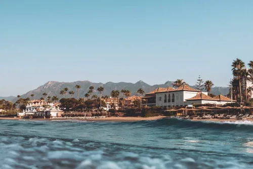 Photographie de Marbella, Entre mer, plage et montagne Photographie artistique de Marbella depuis la mer, plage El Rosario, beach club NOSSO, maisons blanches andalouses, palmiers et montagnes Sierra Blanca sous ciel bleu
