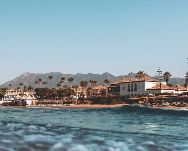 Photographie artistique de Marbella depuis la mer, plage El Rosario, beach club NOSSO, maisons blanches andalouses, palmiers et montagnes Sierra Blanca sous ciel bleu