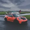 Porsche 911 GT3 RS orange sur piste d'aviation avec avion Beechcraft Bonanza en arrière-plan, photographie d'art automobile