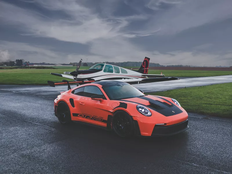 Porsche 911 GT3 RS orange sur piste d'aviation avec avion Beechcraft Bonanza en arrière-plan, photographie d'art automobile