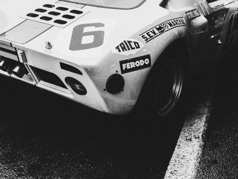 Photographie noir et blanc de l'arrière d'une Ford GT40 de course numéro 6 avec sponsors Ferodo et Koni, sur piste mouillée