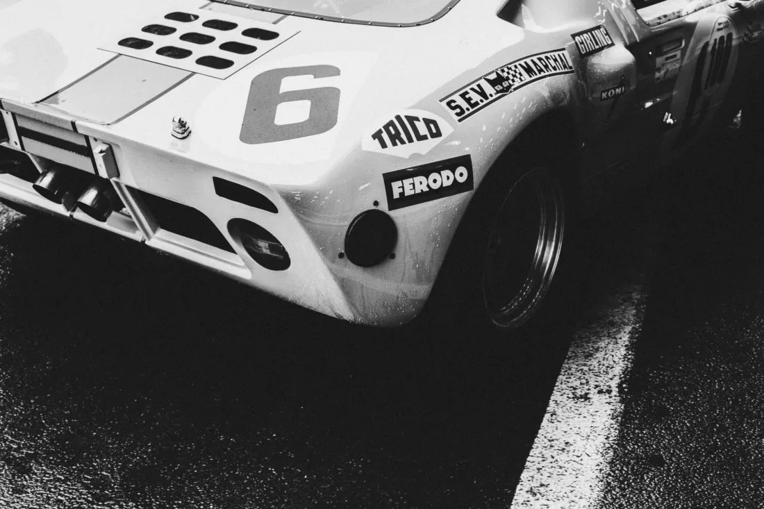 Photographie noir et blanc de l'arrière d'une Ford GT40 de course numéro 6 avec sponsors Ferodo et Koni, sur piste mouillée