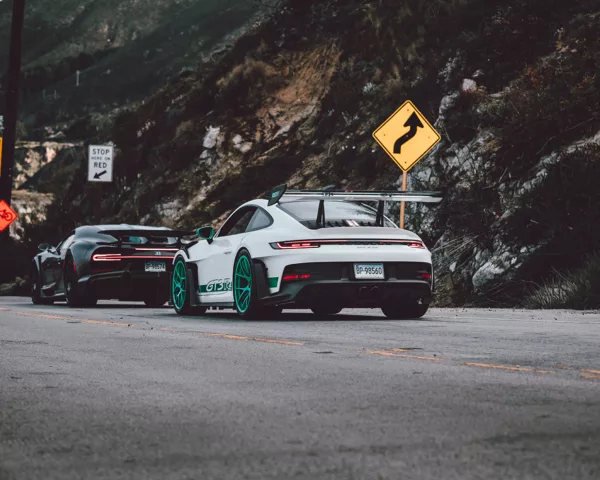 Photo déco murale de Porsche GT3 RS blanche avec jantes turquoise et Bugatti Chiron noire sur route de canyon, parfaite pour décoration intérieure automobile de luxe