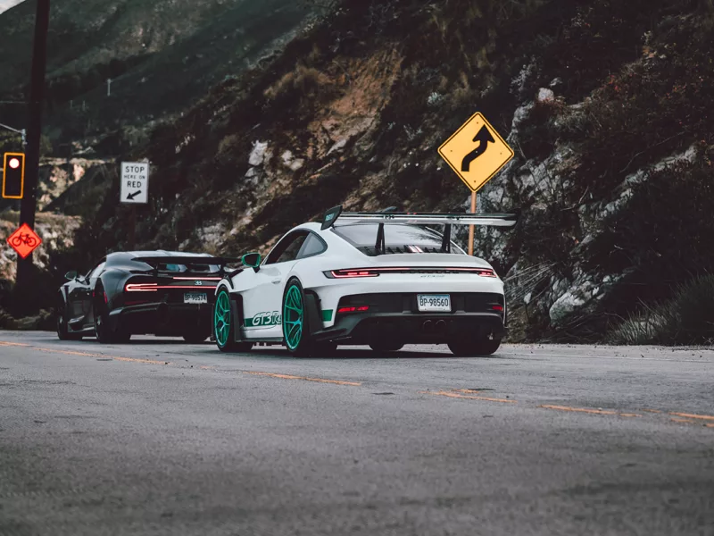 Photo déco murale de Porsche GT3 RS blanche avec jantes turquoise et Bugatti Chiron noire sur route de canyon, parfaite pour décoration intérieure automobile de luxe
