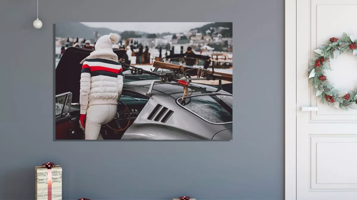 Tableau artistique d'une personne en tenue hivernale blanche près d'une voiture classique, affiché dans un intérieur décoré pour Noël avec couronne et cadeaux - Photographie automobile Cars and Roses