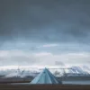 Photographie de paysage du Svalbard montrant une tente tipi bleue solitaire face aux montagnes enneigées des fjords arctiques sous un ciel dramatique