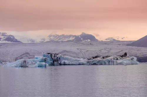 Photographie Islande Glacier Sunset Photographie déco murale du glacier Jökulsárlón en Islande montrant des icebergs bleu azur flottant sur le lagon glaciaire sous un ciel crépusculaire rose, parfaite pour une décoration intérieure scandinave