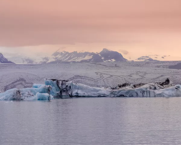 Photographie déco murale du glacier Jökulsárlón en Islande montrant des icebergs bleu azur flottant sur le lagon glaciaire sous un ciel crépusculaire rose, parfaite pour une décoration intérieure scandinave