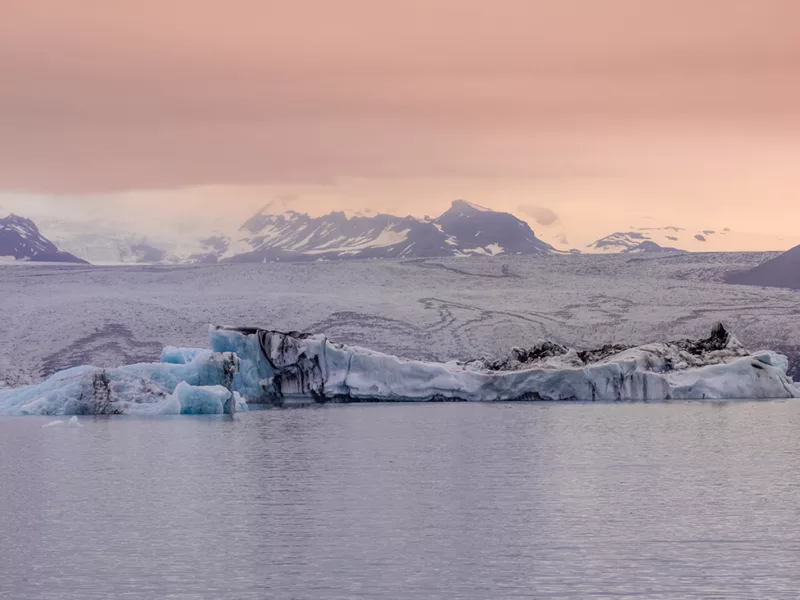 Photographie déco murale du glacier Jökulsárlón en Islande montrant des icebergs bleu azur flottant sur le lagon glaciaire sous un ciel crépusculaire rose, parfaite pour une décoration intérieure scandinave