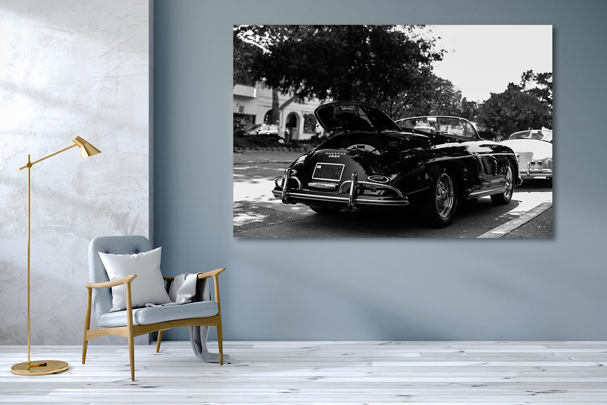 Voiture ancienne décapotable noire garée en plein-air, vue arrière, entourée d’autres voitures, en noir et blanc.