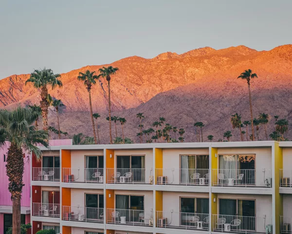 Hôtel The Saguaro avec façades colorées rose orange jaune au coucher de soleil avec montagnes San Jacinto et palmiers à Palm Springs Californie