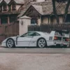 Ferrari F40 grise supercar vue de profil avec aileron arrière iconique et prises d'air latérales, photographiée devant une architecture européenne rustique avec clôture en bois et bâtiments traditionnels