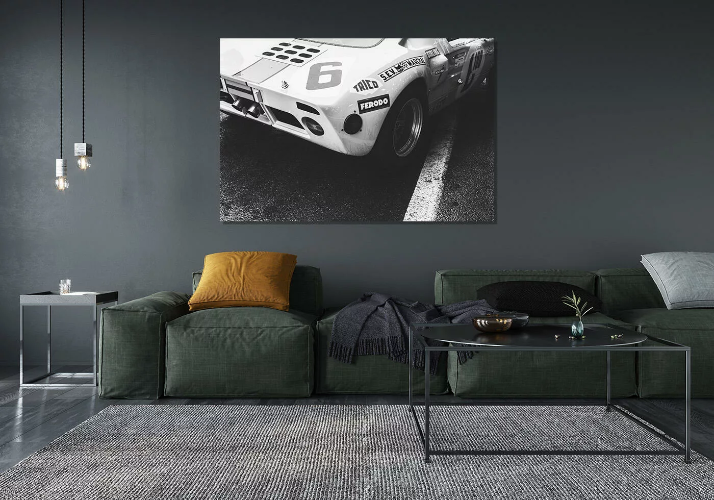 poster voiture noir et blanc, voiture de course accrochée au mur d'un salon moderne, avec canapé vert, tapis gris et lampe suspendue.