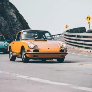 Deux Porsche anciennes en conduite sur une route côtière, l’une jaune au premier plan et l’autre bleue en arrière-plan, dans un virage près d’une rambarde. Comment photographier des voitures anciennes.