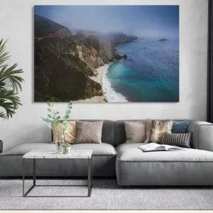 Grand salon moderne avec un canapé gris, table basse et plante d’intérieur, et un paysage côtier imprimé accroché au mur. mur de cadres photos décoration, cadre central dominé par la mer.