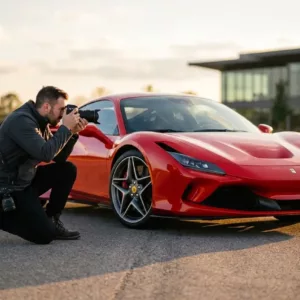 Photographe près d’une Ferrari rouge, prenant des photos de l’intérieur et de la carrosserie, illustrant la meilleure focale pour la photographie automobile.