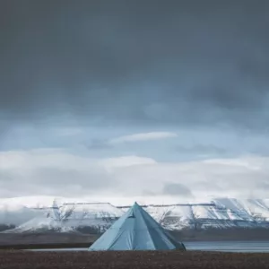 Tente bleue sur une plage glacée avec montagnes enneigées au loin, idéal pour apprendre comment prendre une belle photo de paysage.