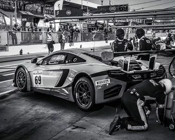 Voiture de course en pit-stop, technician en train de vérifier les réglages sous une imposante aile arrière, ambiance garage et spectateurs en arrière-plan. intégration: meilleure focale pour la photographie automobile