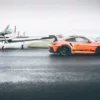 Piste Mouillée Wall ARt Porsche GT3 Rs Porsche GT3 RS orange sur piste mouillée face à un avion léger - tableau photographique d'art