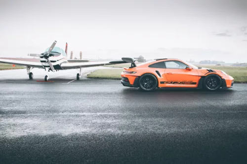 Piste Mouillée Wall ARt Porsche GT3 Rs Porsche GT3 RS orange sur piste mouillée face à un avion léger - tableau photographique d'art