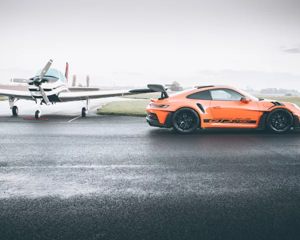Porsche GT3 RS orange sur piste mouillée face à un avion léger - tableau photographique d'art