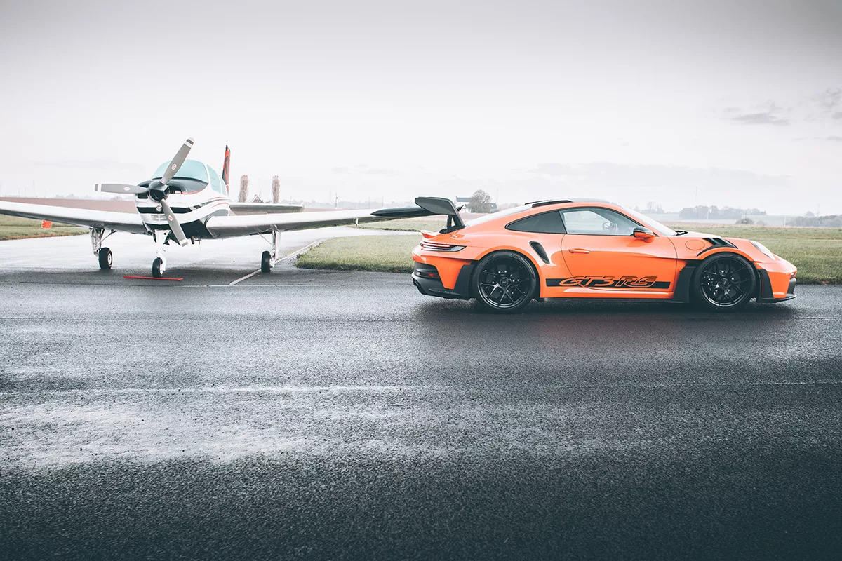 Porsche GT3 RS orange sur piste mouillée face à un avion léger - tableau photographique d'art