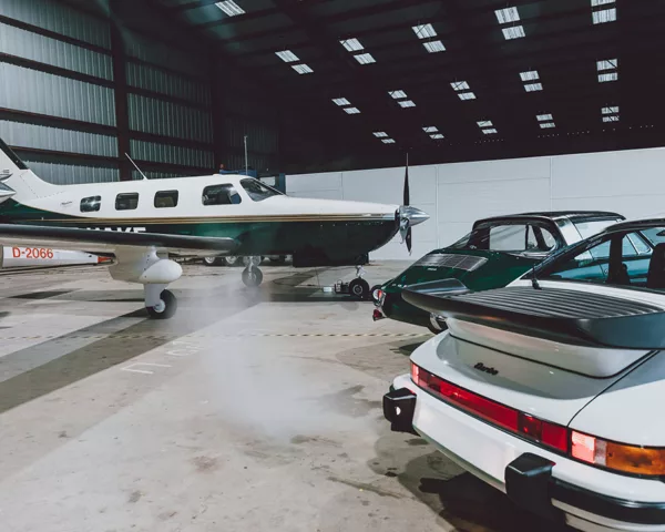 Porsche 911 Turbo blanche et 911 verte devant un Piper Malibu dans un hangar éclairé par des verrières - tableau photographique d'art