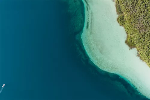 Photographie aérienne du lac de Kournas en Crète : eau bleu profond, hauts-fonds turquoise et petit bateau